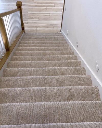 The image captures the detail of a well-designed modern staircase, lined with plush beige carpet, complemented by white walls and wooden balusters.
